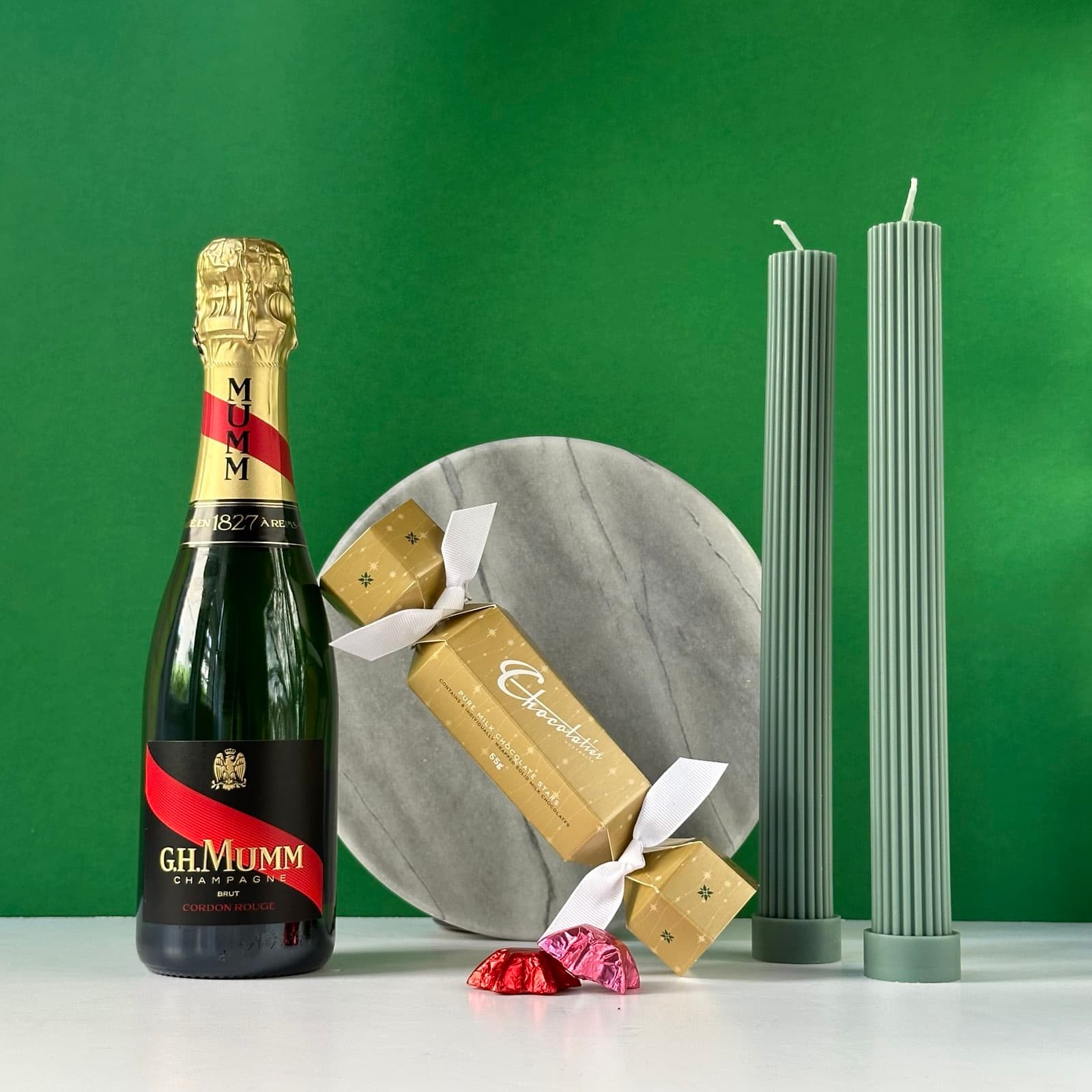 A festive gift bundle featuring G.H. Mumm champagne, gold bon bon chocolates, sage green pillar candles, and a marble serving plate, all elegantly packaged in a premium Thankly box.